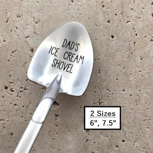 May include: A silver-colored metal spoon shaped like a shovel with the text DAD'S ICE CREAM SHOVEL engraved on the bowl. A rectangular box indicates 2 Sizes 6", 7.5" are available for this utensil, which features a smooth, polished finish.
