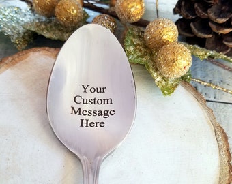 May include: A silver spoon with a personalized message that reads "Your Custom Message Here". The spoon is on a wooden surface with gold-colored ornaments.