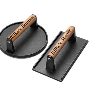 May include: Two cast iron burger and steak presses with wooden handles. The handles are engraved with "Mike's Burgers" and "Mike's Steaks".