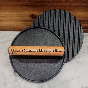 May include: A black cast iron grill press with a wooden handle. The handle is engraved with the text "Your Custom Message Here".