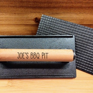 May include: A black cast iron grill press with a wooden handle. The handle has the text "JOE'S BBQ PIT" engraved on it.