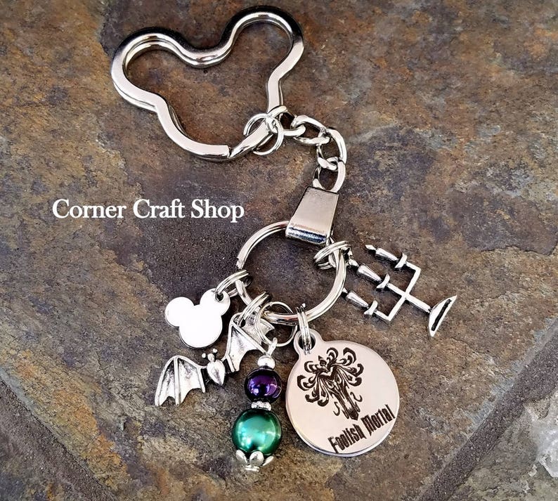 May include: Silver keychain with a Mickey Mouse charm, a bat charm, a green bead, a purple bead, and a round charm with a black and white image of a tree and the text "Foolish Mortal".
