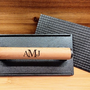 May include: A black cast iron grill press with a wooden handle. The handle has the initials "AMJ" engraved on it.