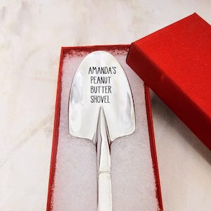 May include: A silver peanut butter shovel with the text "Amanda's Peanut Butter Shovel" engraved on the front. The shovel is in a red box with white lining.