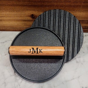 May include: A set of two black cast iron grill press with a wooden handle engraved with the initials "JMK".