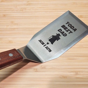 May include: A stainless steel spatula with a wooden handle. The spatula has a Yoda character and the text "Yoda Best Dad" and "Jacob & Justin" engraved on it.
