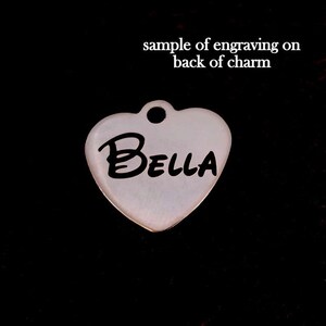 May include: A white heart-shaped charm with the name "Bella" engraved in black lettering. This is a sample of engraving on the back of the charm.
