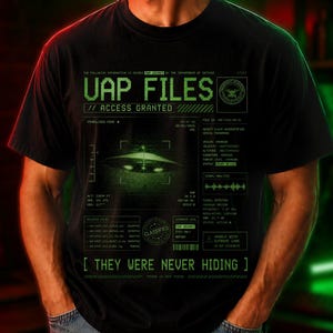 May include: Black t-shirt with green text and graphics. The shirt features the text "UAP FILES // ACCESS GRANTED" and a graphic of a UFO. Below the graphic is the text "[ THEY WERE NEVER HIDING ]".