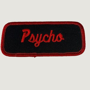 Etiqueta de identificação vintage com bordado "Psycho Script" em preto e vermelho, estilo motociclista/trabalho.