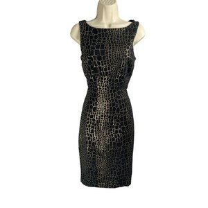 May include: Sleeveless black dress with a gold, textured pattern. The dress has a scoop neckline and a fitted silhouette, showcasing a unique design. The dress is displayed on a mannequin.