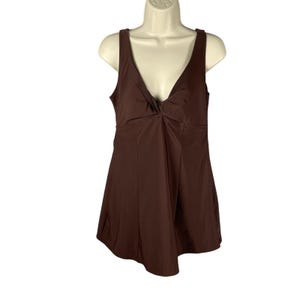 May include: A brown one-piece swimsuit with a V-neckline and a knotted detail at the bust. The swimsuit has a sleeveless design and a skirted bottom. The garment is displayed on a white mannequin against a white background.