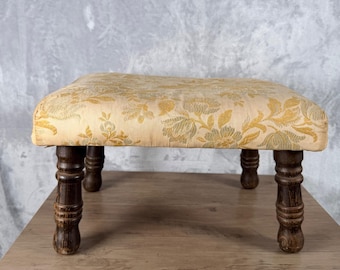 Poggiapiedi vintage in broccato floreale con gambe in legno a fuso, color oro e marrone chiaro, con rivestimento in tessuto.