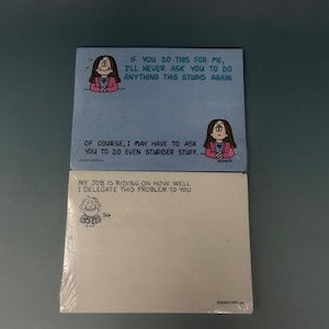 May include: Two pads of sticky notes. The top pad is blue with a cartoon drawing of a woman and the text: "IF YOU DO THIS FOR ME, I'LL NEVER ASK YOU TO DO ANYTHING THIS STUPID AGAIN." The bottom pad is white with a cartoon drawing and the text: "MY JOB IS RIDING ON HOW WELL I DELEGATE THIS PROBLEM TO YOU."