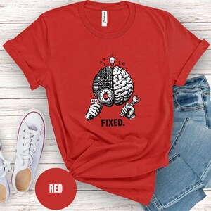 May include: A red short-sleeved t-shirt featuring a graphic of a brain split between a circuit board and organic tissue. The design includes a magnifying glass over a bug, a wrench, a lightbulb, binary code, and the text "404" and "FIXED."
