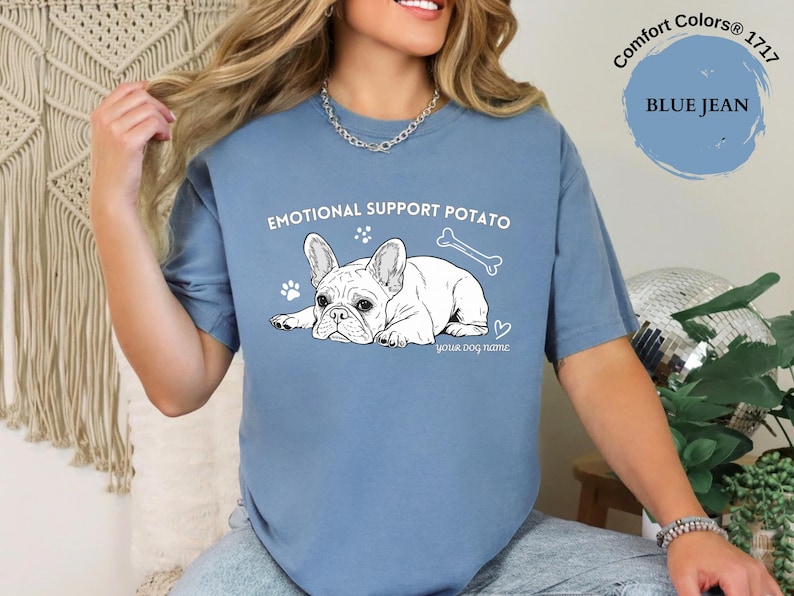 May include: Blue jean Comfort Colors t-shirt featuring a French Bulldog graphic and the text "EMOTIONAL SUPPORT POTATO". The design includes a bone, paw prints, and a heart. The text "your dog name" is below the dog.