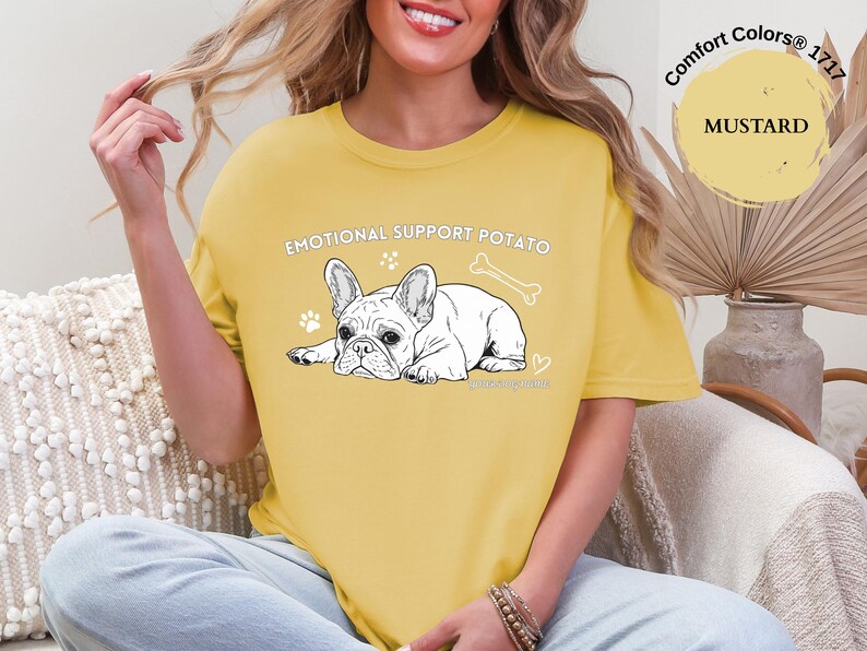 May include: Mustard yellow t-shirt featuring the text "EMOTIONAL SUPPORT POTATO" and a black and white illustration of a French Bulldog. The design includes a bone, paw prints, and a heart.
