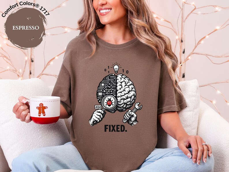 May include: An espresso brown short-sleeve t-shirt featuring a graphic of a brain split between a circuit board and organic tissue. One hand holds a magnifying glass over a red bug, while the other holds a wrench. Text reads 404 and FIXED.