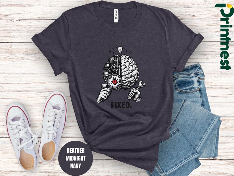 May include: A heather midnight navy t-shirt featuring a graphic of a brain split into a circuit board and organic side. One hand holds a magnifying glass over a red bug, while the other holds a wrench. Above is a lightbulb and the text FIXED.