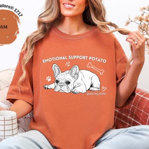May include: A burnt orange Comfort Colors t-shirt with the words "EMOTIONAL SUPPORT POTATO" and a white illustration of a French Bulldog. The shirt also features a bone, paw prints, and a heart graphic.