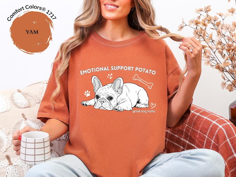 May include: A burnt orange Comfort Colors t-shirt with the words "EMOTIONAL SUPPORT POTATO" and a white illustration of a French Bulldog. The shirt also features a bone, paw prints, and a heart graphic.