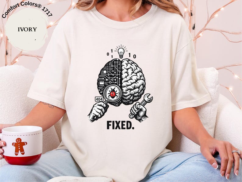 May include: An ivory t-shirt featuring a graphic of a brain split between a circuit board and organic tissue. One hand holds a magnifying glass over a red bug with a 404 label, while the other holds a wrench. A lightbulb and binary code appear above.