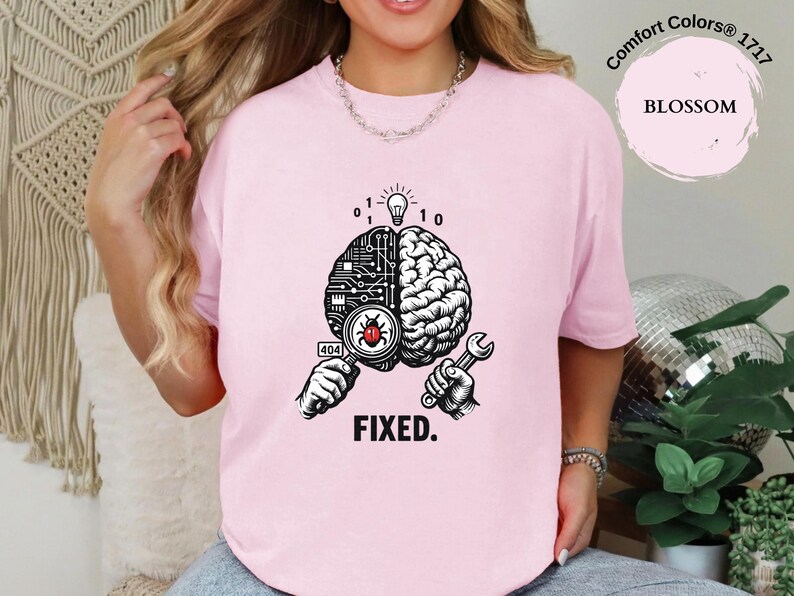 May include: A light pink t-shirt featuring a graphic of a split brain, with one side showing circuit board patterns and the other side showing organic brain tissue. A magnifying glass reveals a red bug, and the text reads 404 and FIXED.