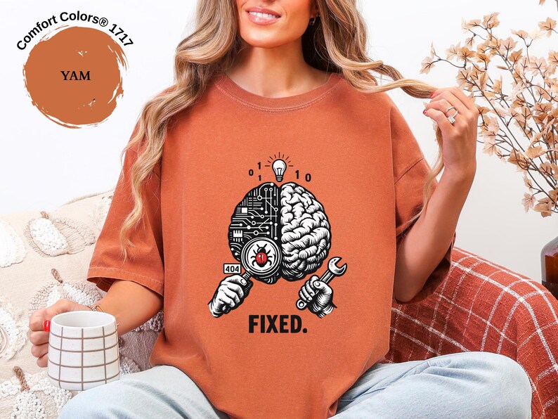May include: A yam-colored t-shirt featuring a graphic of a brain split between a circuit board and organic tissue. The design includes a magnifying glass over a bug, a wrench, binary code, a lightbulb, and the text "404" and "FIXED."