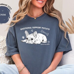 May include: Denim blue t-shirt featuring a French Bulldog graphic and the text "EMOTIONAL SUPPORT POTATO". The design includes a bone, paw prints, and a heart. The shirt is a Comfort Colors 1717.