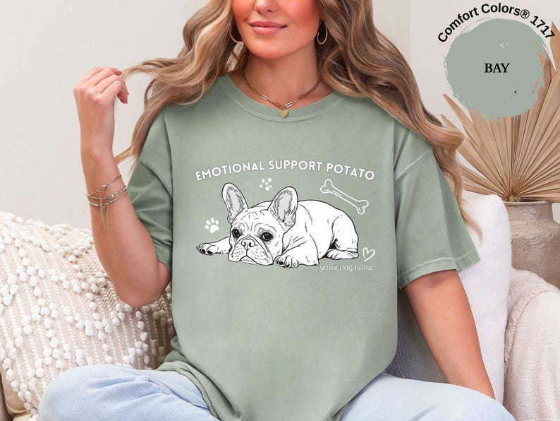 May include: Sage green t-shirt featuring the text "EMOTIONAL SUPPORT POTATO" and a black and white illustration of a French Bulldog. The design includes paw prints, a bone, and a heart.