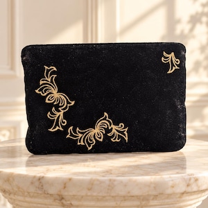 May include: A rectangular black velvet pouch featuring gold embroidered scrollwork patterns. The embroidery is positioned on the left side and the bottom center, with a smaller matching gold embroidered motif located in the top right corner.