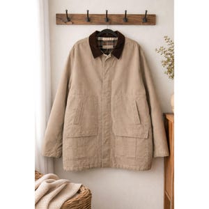 May include: A tan-colored jacket with a brown corduroy collar and a plaid lining. The jacket has two large front pockets and is hanging on a wooden rack with black hooks. The jacket is a neutral color and suitable for various outfits.