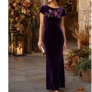 May include: A floor-length deep purple velvet dress featuring short sleeves and a round neckline. The bodice is adorned with an intricate floral embroidery pattern in shades of pink, red, and gold, creating a textured and detailed visual accent.