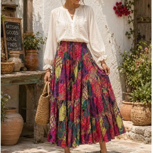 May include: A long-sleeved white blouse with a V-neckline and lace detailing paired with a tiered, floor-length skirt featuring a vibrant, multi-colored patchwork pattern in shades of pink, purple, and green, complete with a drawstring waist.