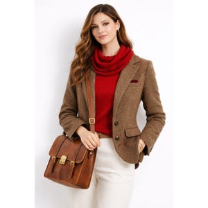 Puede incluir: Blazer de tweed marrón, jersey rojo y bolso bandolera de cuero marrón. El bolso tiene forma rectangular con dos hebillas y una correa para el hombro. La blazer tiene un pañuelo de bolsillo y un corte clásico.