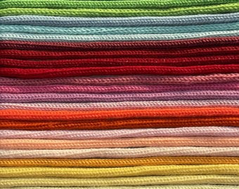 May include: A close-up of a collection of colorful cords, arranged horizontally. The cords are in a variety of colors, including purple, blue, green, red, orange, and yellow. The cords appear to be made of a woven material.