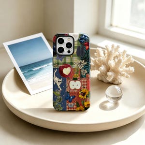 May include: A smartphone case featuring a vibrant collage design with a red apple, a white cat wearing sunglasses, a blue butterfly, yellow sunflowers, a bee, and various checkered and solid coloured patterns in shades of red, blue, and green.