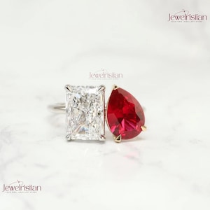 May include: Two rings with large gemstones. One ring features a rectangular, clear gemstone. The other ring has a pear-shaped, deep red gemstone. Both rings are set on silver bands. The brand name "jewelrisiian" is visible in the top right and bottom left corners.