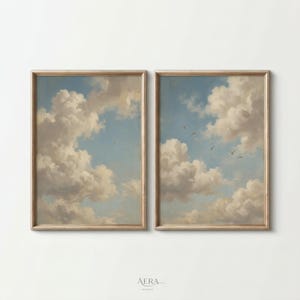 Könnte beinhalten: Zwei gerahmte Landschaftsbilder zeigen einen hellblauen Himmel voller flauschiger weißer Wolken. Das Kunstwerk hat eine Vintage-Ästhetik, mit Vögeln am Himmel. Die Rahmen sind hellbraun und die Gemälde sind vor weißem Hintergrund ausgestellt.
