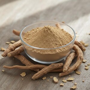 May include: A clear glass bowl filled with light brown powder, surrounded by several pieces of dried, brown root. The bowl sits on a wooden surface, with small pieces of the root scattered around.