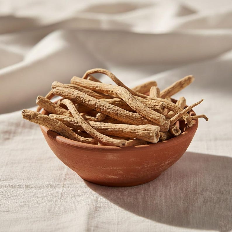 May include: A terracotta bowl filled with dried, beige-colored roots. The roots are of varying lengths and textures, with some curved and others straight. The bowl sits on a light-colored, textured fabric, with soft lighting creating shadows.