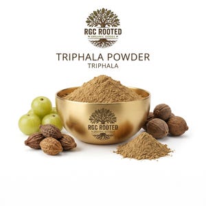 Könnte beinhalten: Eine goldfarbene Schale gefüllt mit hellbraunem Triphala-Pulver, versehen mit dem Logo RGC Rooted Organic Goods. Neben der Schale liegen grüne Amla-Früchte und getrocknete braune Haritaki-Früchte, mit einem kleinen Häufchen Pulver im Vordergrund.