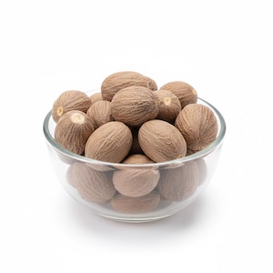 May include: A glass bowl filled with whole nutmegs. The nutmegs are light brown with textured surfaces. The bowl is set against a white background, highlighting the spices.