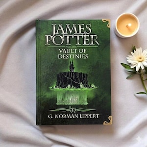 May include: A hardcover book titled James Potter and the Vault of Destinies by G. Norman Lippert. The cover is dark green with a black illustration of a cliffside structure, gold corner accents, and white text. A small candle and flower are nearby.