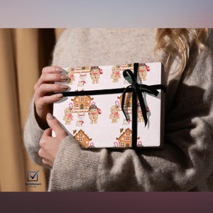 Może przedstawiać: Zapakowane pudełko prezentowe z powtarzającym się wzorem piernikowych domków i ludzików. Pudełko jest zawiązane czarną aksamitną wstążką. Motyw jest świąteczny i odpowiedni na święta.