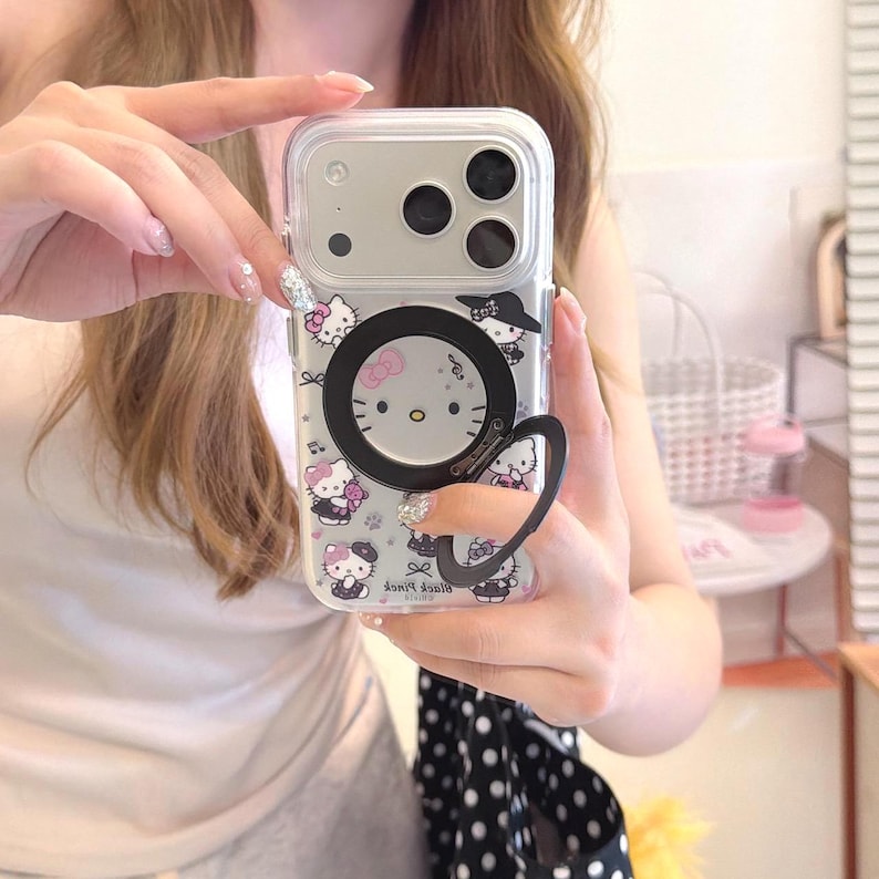K&ouml;nnte beinhalten: Transparente Handyh&uuml;lle mit einem Hello Kitty-Design und einem schwarzen Ringhalter. Die H&uuml;lle hat eine transparente R&uuml;ckseite mit mehreren Hello Kitty-Illustrationen. Der Ringhalter ist an der R&uuml;ckseite der Handyh&uuml;lle befestigt.