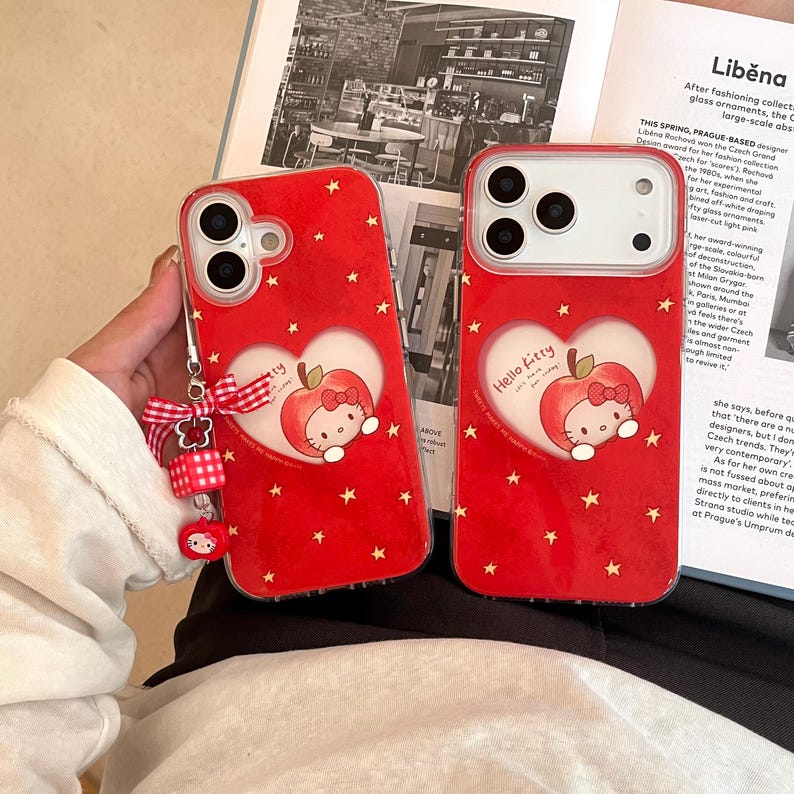 Puede incluir: Dos fundas rojas para tel&eacute;fono con un dise&ntilde;o de Hello Kitty. Cada funda presenta un gr&aacute;fico en forma de coraz&oacute;n con una manzana y Hello Kitty. Las fundas est&aacute;n cubiertas de peque&ntilde;as estrellas doradas. Una funda tiene un dije con un lazo y una figura de Hello Kitty.