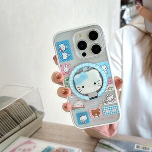 Puede incluir: Funda transparente para tel&eacute;fono con dise&ntilde;o de Hello Kitty. La funda presenta un soporte de anillo azul con una cara de Hello Kitty y varias pegatinas de personajes de dibujos animados. La funda est&aacute; dise&ntilde;ada para un tel&eacute;fono inteligente.