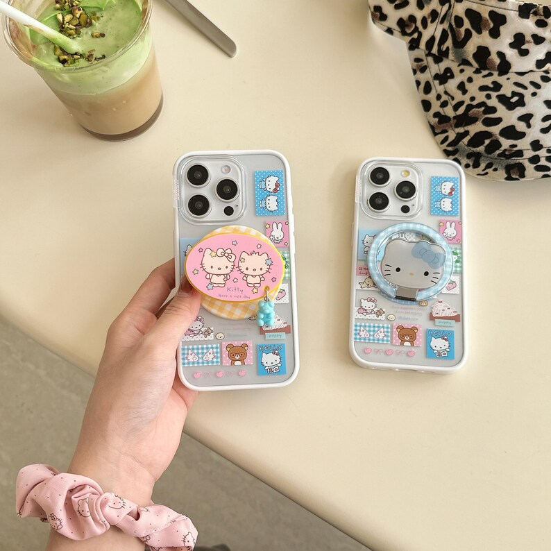 Puede incluir: Dos fundas transparentes para tel&eacute;fono con dise&ntilde;os coloridos de Hello Kitty. Una funda tiene un soporte desplegable rosa y amarillo con dos personajes de Hello Kitty. La otra funda tiene un soporte de anillo azul con una cara de Hello Kitty.