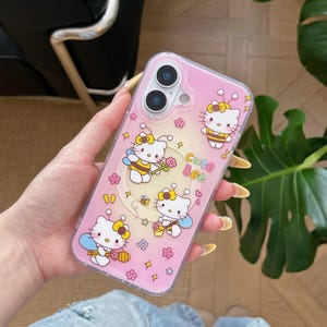 May include: Pink phone case featuring a cartoon design with Hello Kitty characters dressed as bees. The case has a clear border and includes the text "Cute Bee" along with floral and star accents. The phone case is designed to fit a smartphone.
