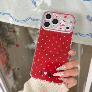 May include: Red phone case with a white star pattern and a clear top section. The top section features a cartoon character and the text "KT I KT I". The case has a circular design on the back and the text "I &hearts; KT".